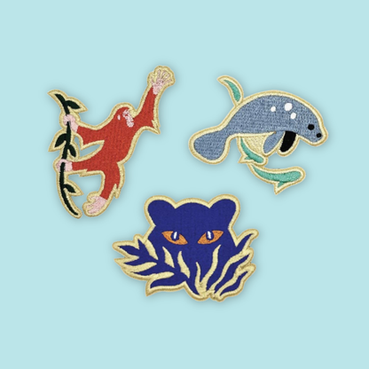 Three colorful animal-themed pins on a light Mandai Wildlife Reserve
